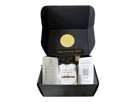A black gift box with a gold VIP sticker on the lid inside the box a white coconut wax melt labeled "Cape Town Countdown" a wax melt care instructions card, a please review us card, and a World Traveler Aroma business Card on a white background.