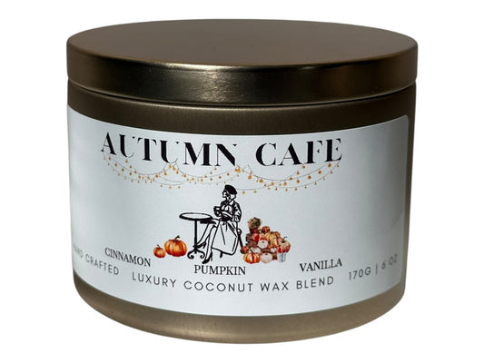 A gold candle tin labeled 'Autumn Cafe' with a decorative label on a white background.