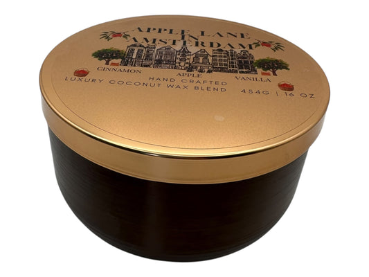 A bronze and gold candle tin labeled "Apple Lane in Amsterdam" with a decorative clear label on a white background.