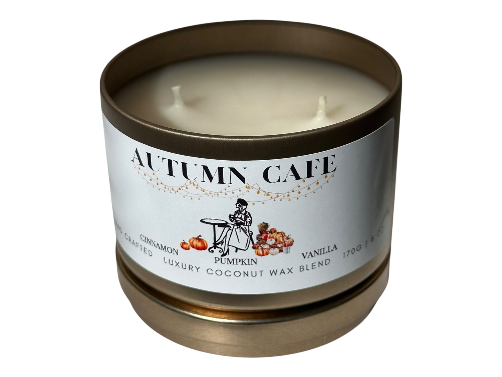 A gold candle tin  with 'Autumn Cafe' label lid removed on a white background