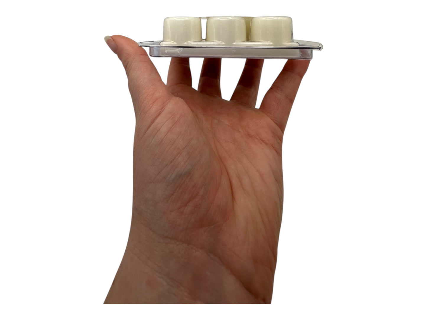 Hand holding a small plastic clamshell  with three white wax melts on a white background