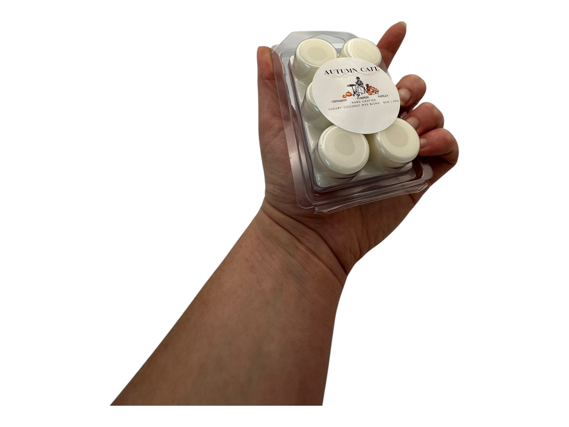 Hand holding a small container of white wax melts with "Autumn Cafe" label on a white background.