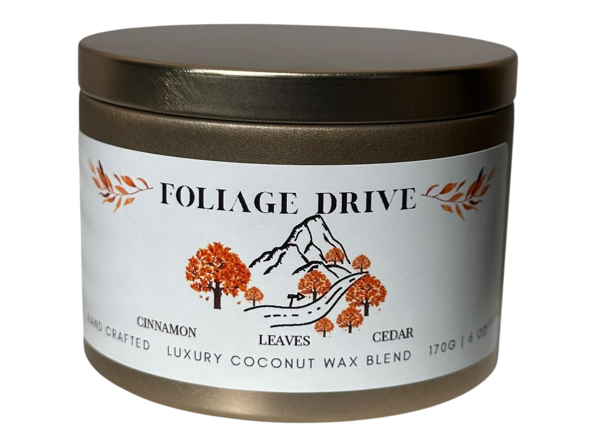 A gold candle tin  labeled 'Foliage Drive' with a mountain and tree design on the label on a white background.