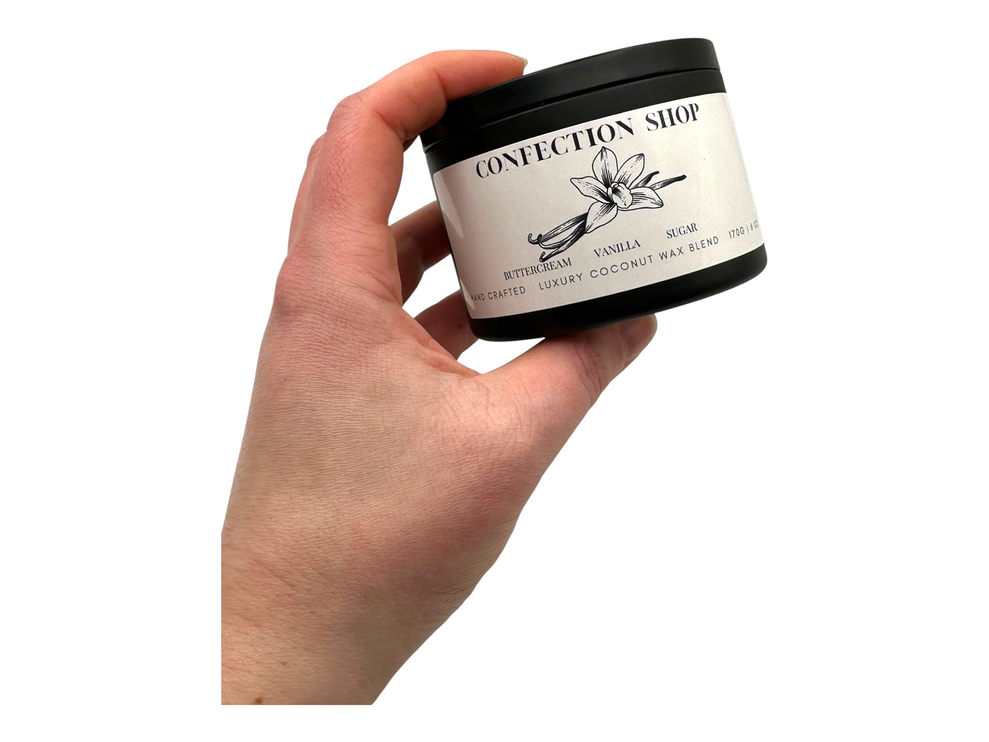 A hand holding a  black candle tin labeled "Confection Shop" on a white background.