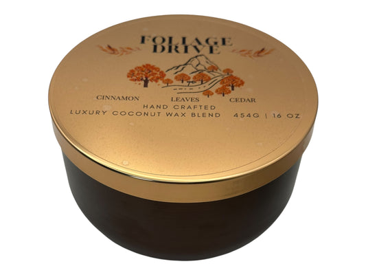 A bronze and gold candle tin labeled "Foliage Drive" with a decorative clear label lid on a white background.