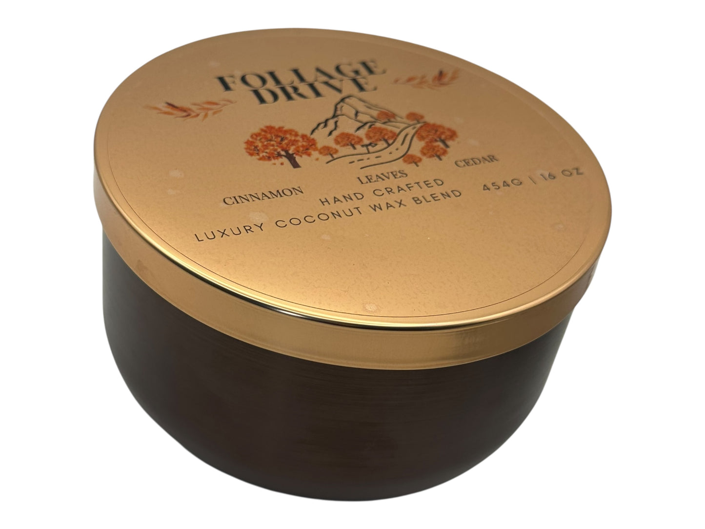 A side view bronze and gold candle tin labeled "Foliage Drive" with a decorative clear label lid on a white background.