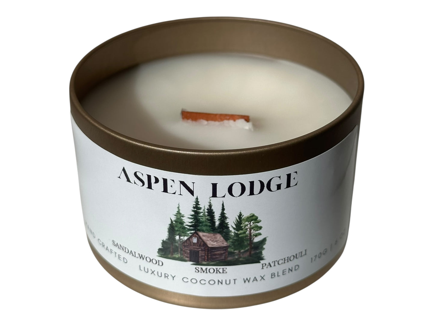 A gold candle tin with lid removed wooden wick and smooth candle top labeled 'Aspen Lodge' on a white background.