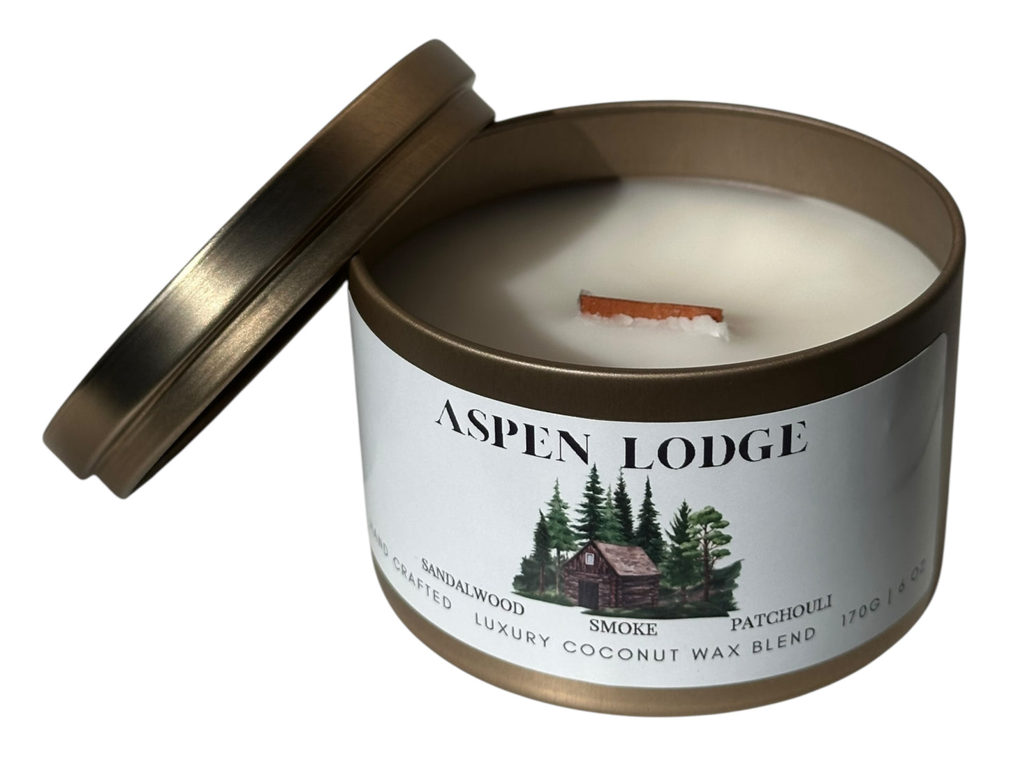 A gold candle tin with lid removed showing a wood wick and a smooth white candle top labeled 'Aspen Lodge' on a white background.