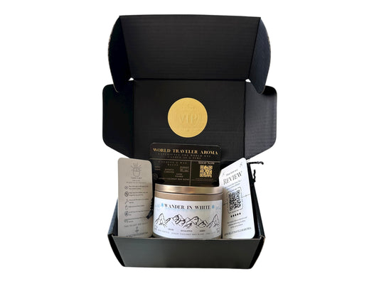 Black gift box with a gold VIP sticker on the lid inside the box a gold candle tin labeled "Wander in White" a candle care card instructions, a please review us card, and a World Traveler Aroma business card on a white background.
