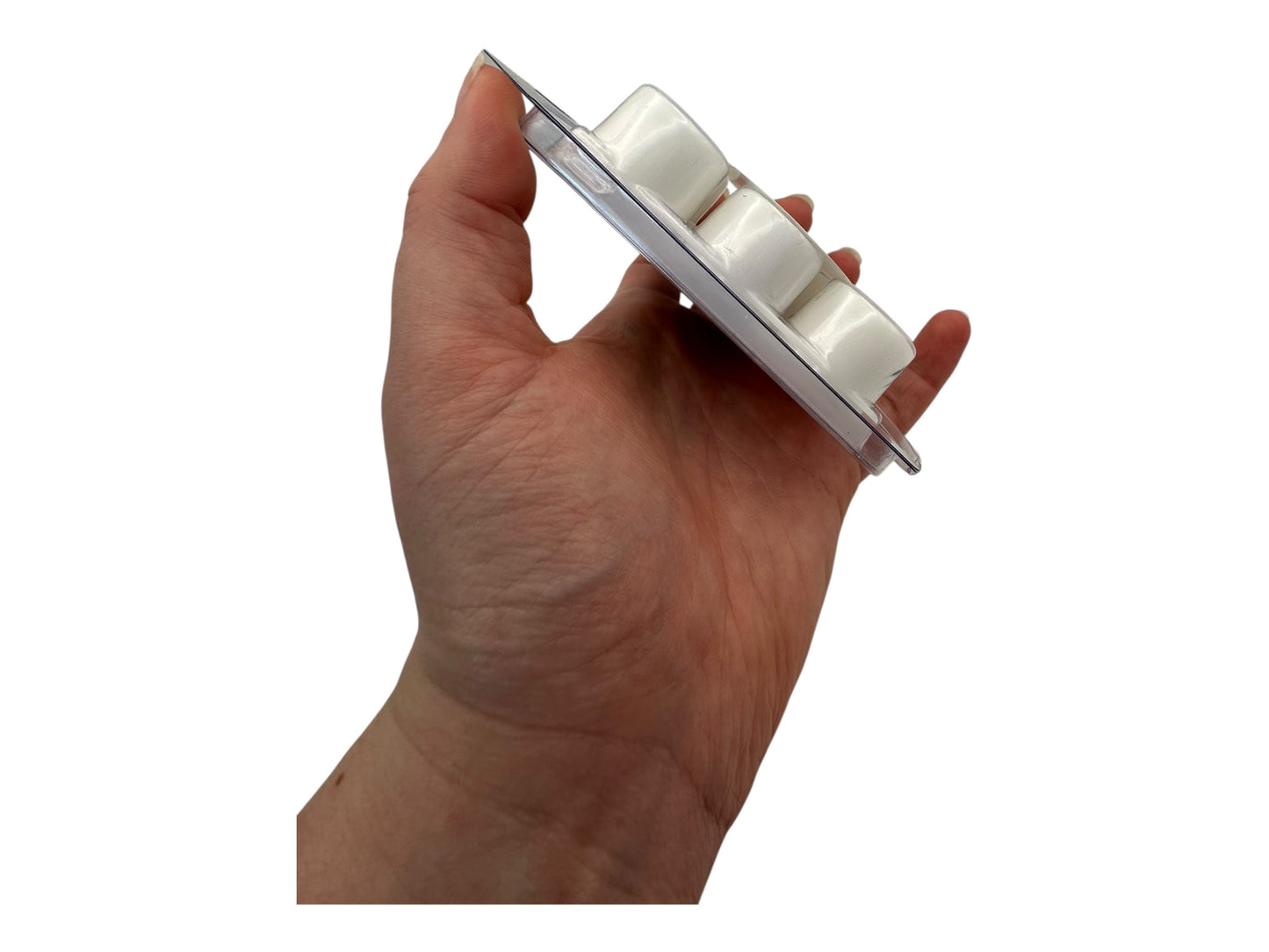 A hand holding white wax melts in a plastic clamshell full side view on a white background.