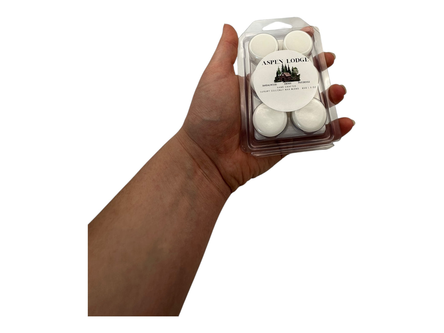 A hand holding a package of Aspen Lodge wax melts against a white background.