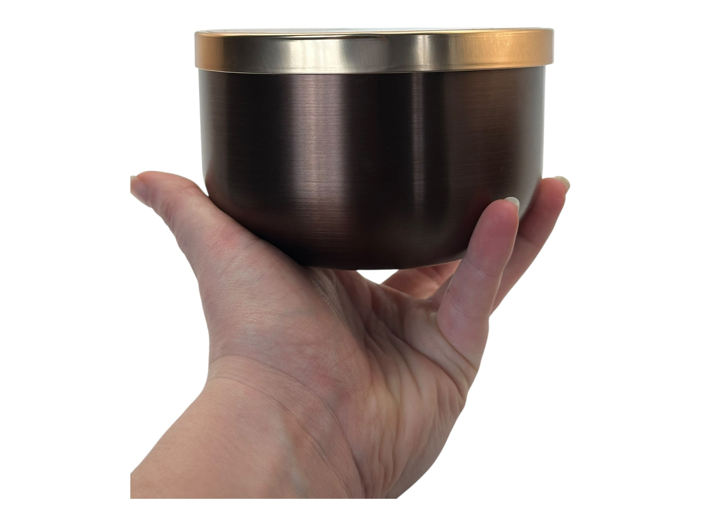 A hand holding a bronze and gold candle tin labeled "Aspen Lodge" on a white background.