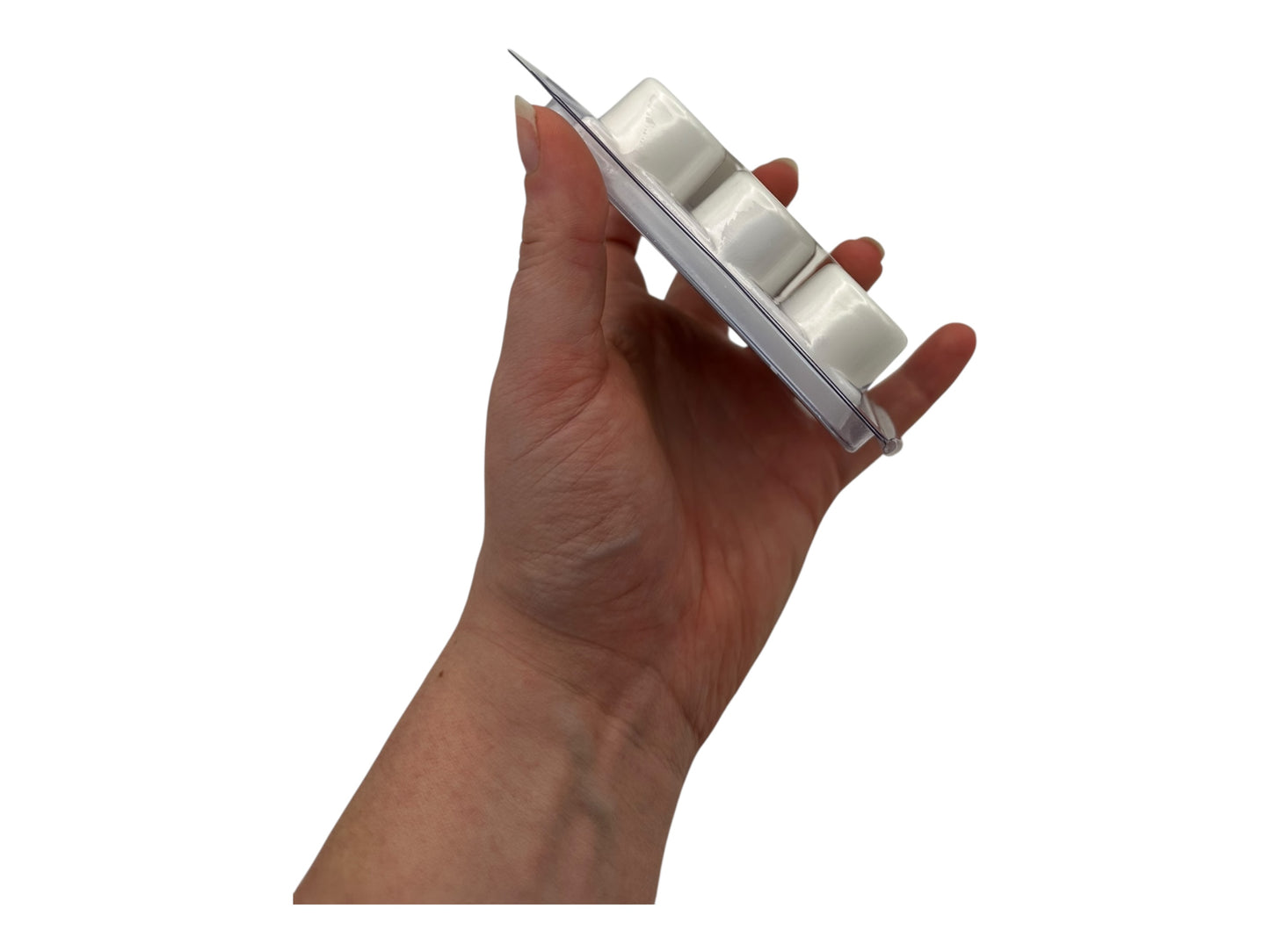 A hand holding white wax melts in a plastic clamshell full side view on a white background.