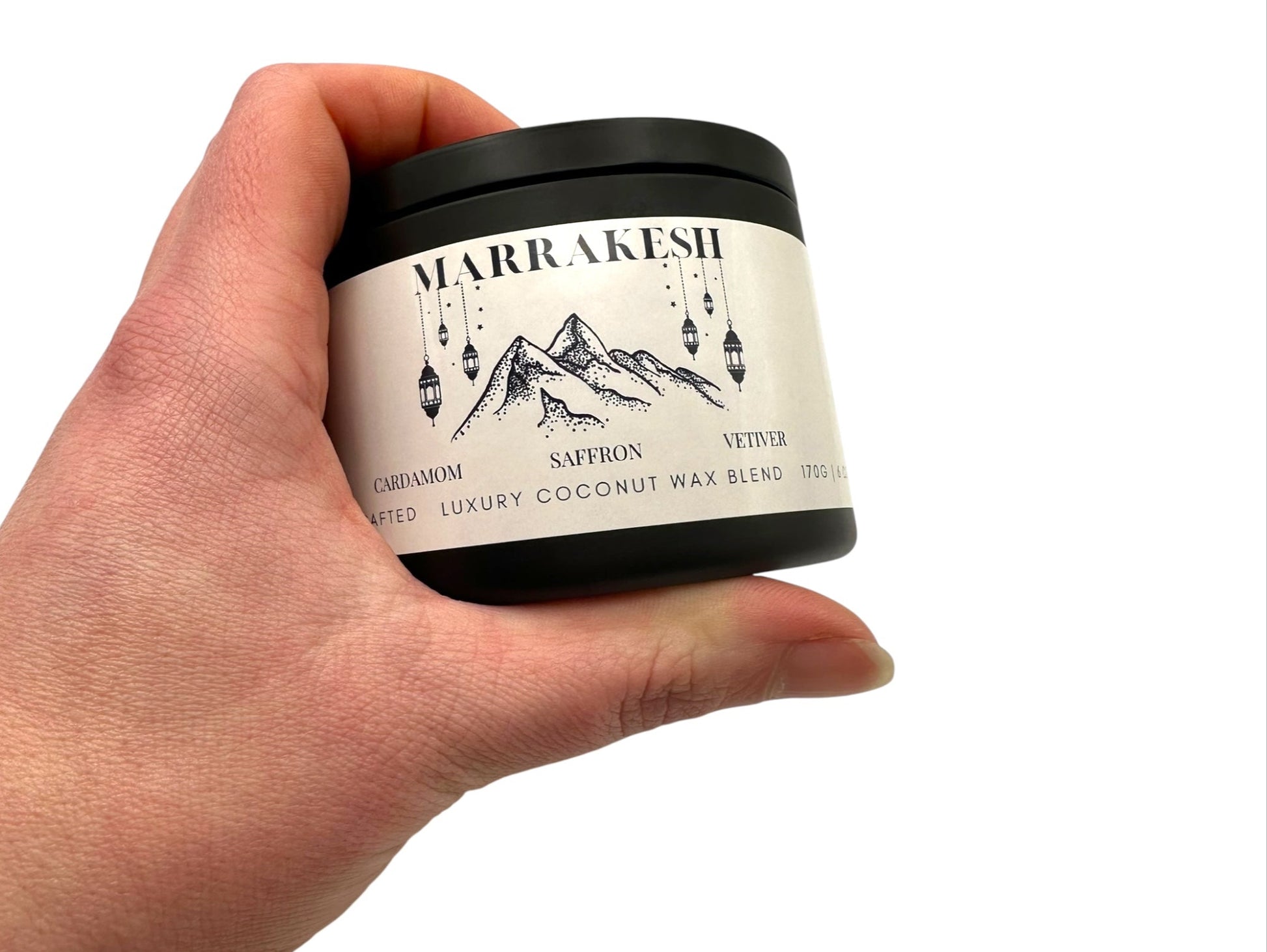 A hand holding black candle tin labeled "Marrakesh" on a white background.