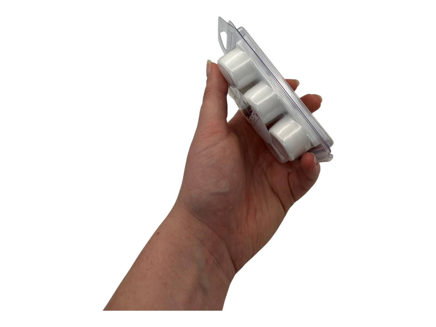 A hand holding white wax melts in a plastic clamshell in full side view on a white background.