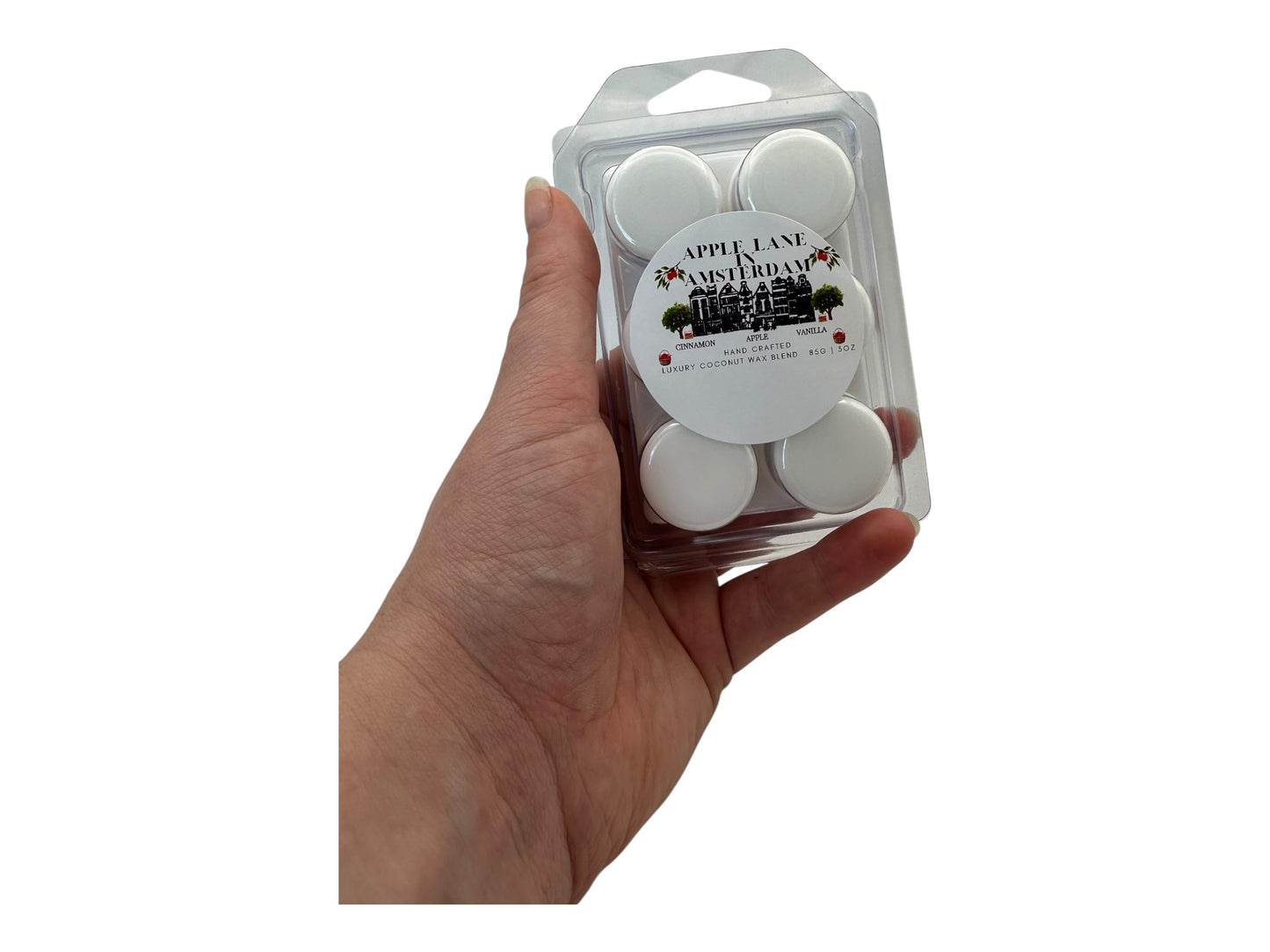 A hand holding "Apple Lane in Amsterdam" wax melts in a plastic clamshell on a white background