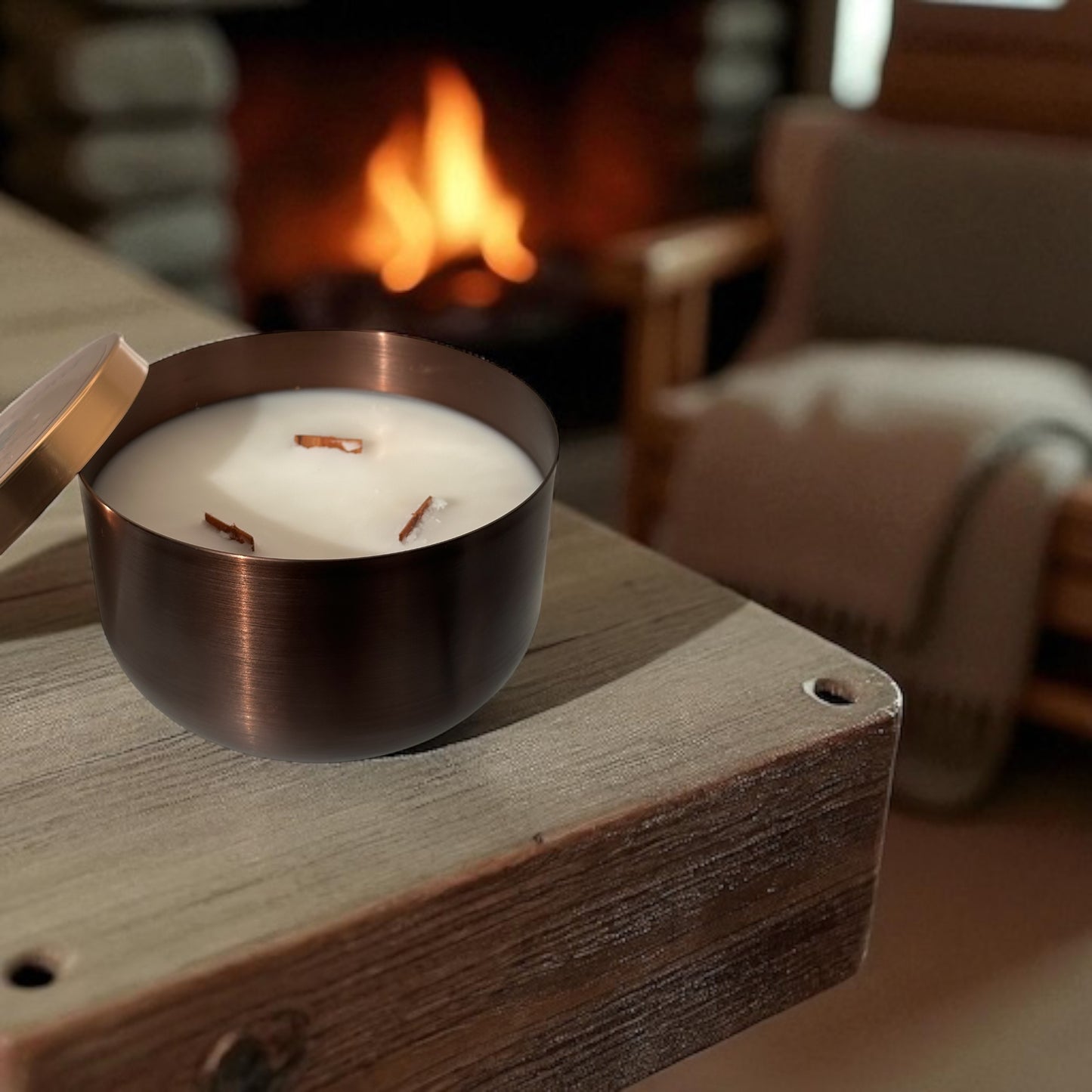 A bronze candle tin on a wooden table with a fireplace and chair in the background