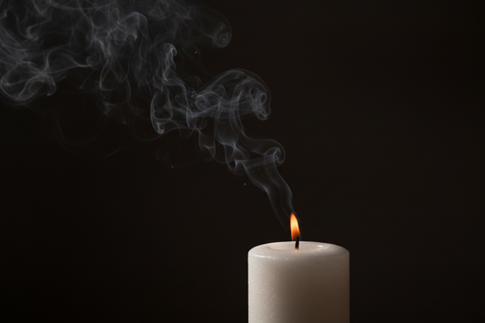 A white candle giving off black smoke while lit