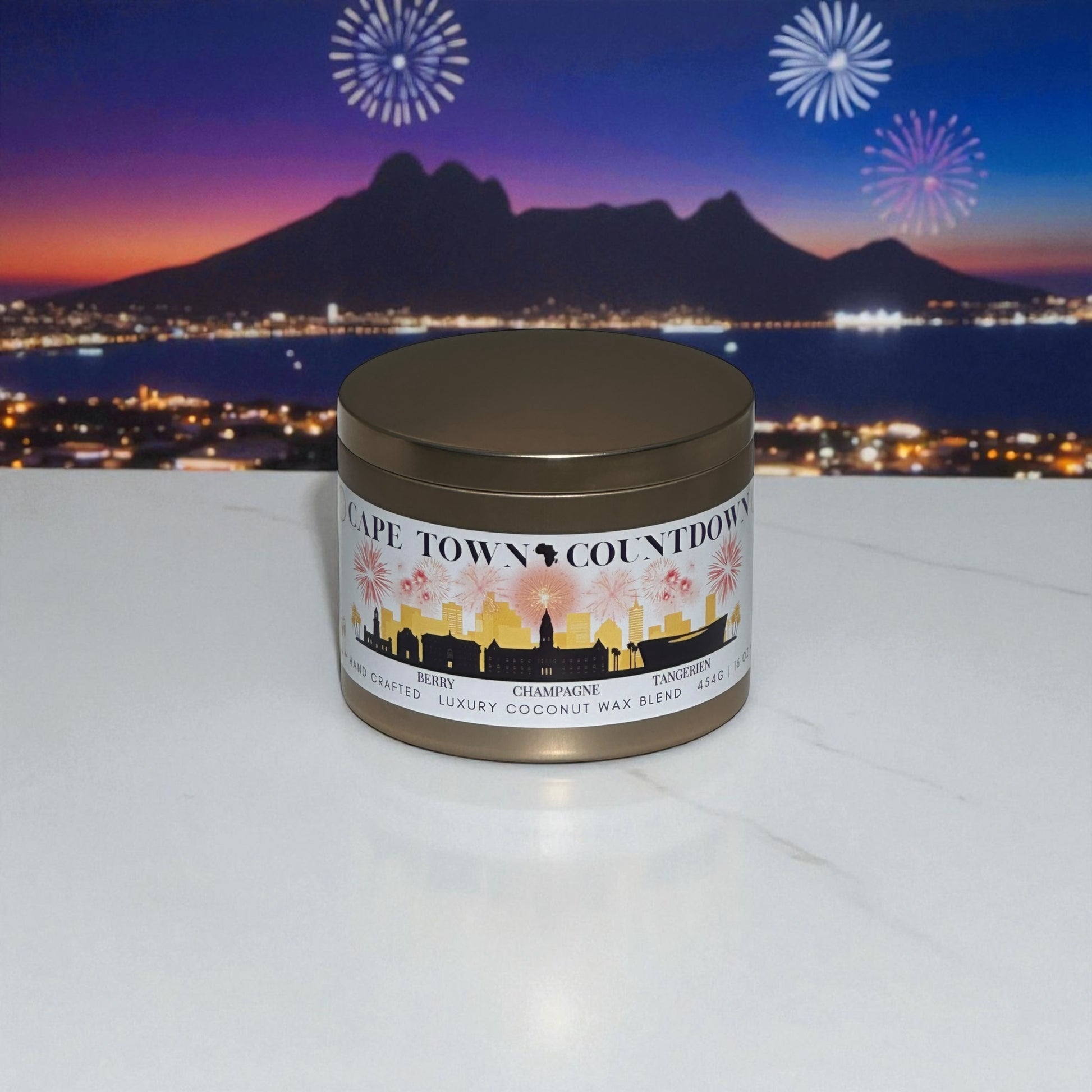 A new year's gold candle tin labeled "Cape Town Countdown" sitting on a marble balcony ledge overlooking Cape Town city scape and dusk with fireworks in the night sky.