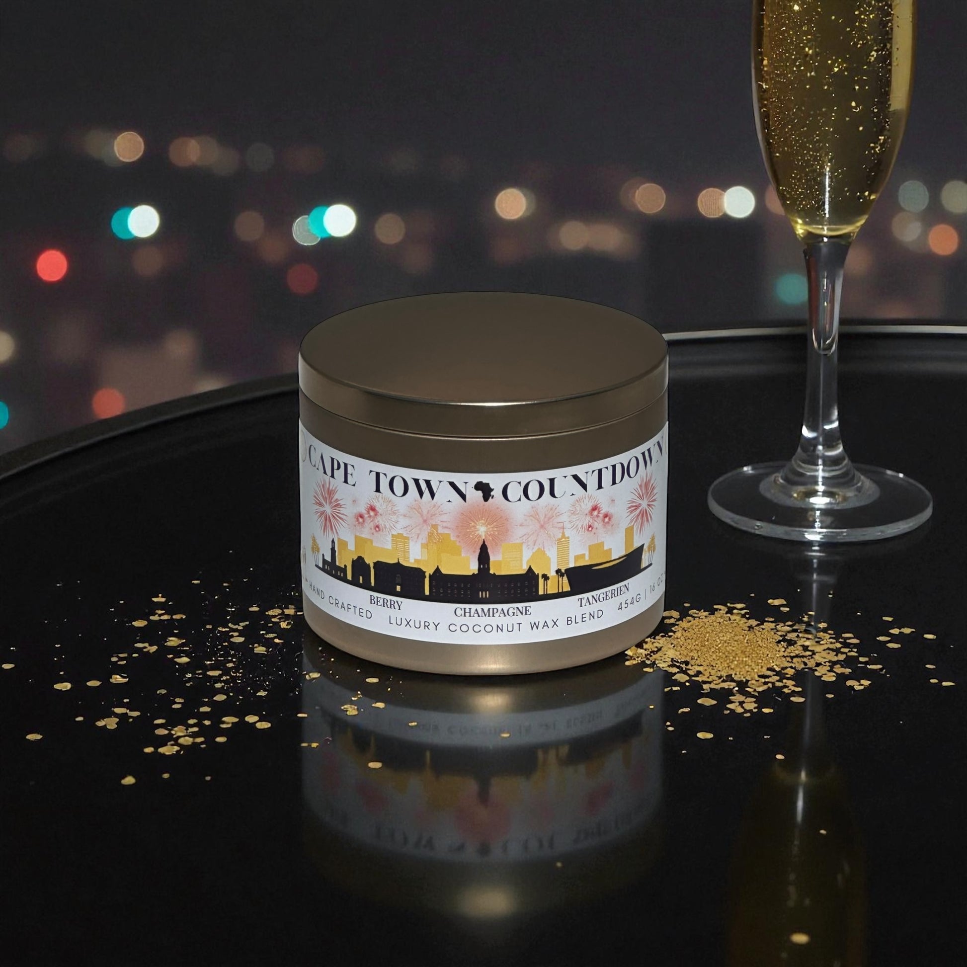 A new year candle tin sitting on a reflective black surface with gold glitter and a glass of champagne flute sitting next to the candle with a night lit city in the background.