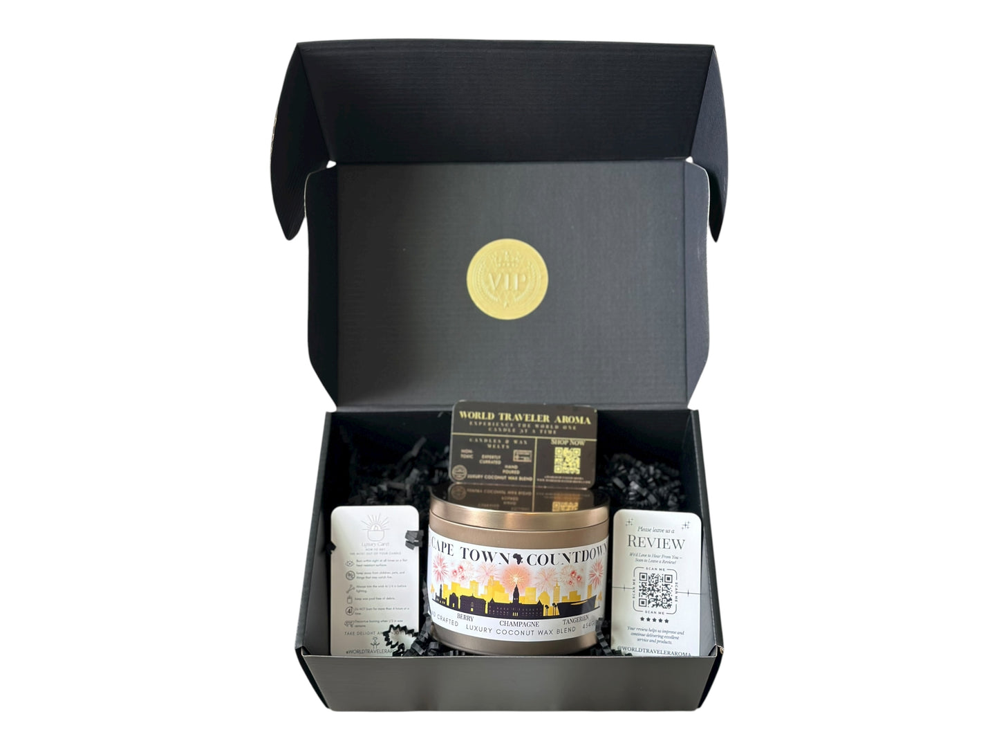 A black gift box with a gold VIP sticker on the lid inside the box a gold candle tin labeled "Cape Town Countdown" with a candle care card instructions, a please review us card, and World Traveler Aroma business card on a white background.