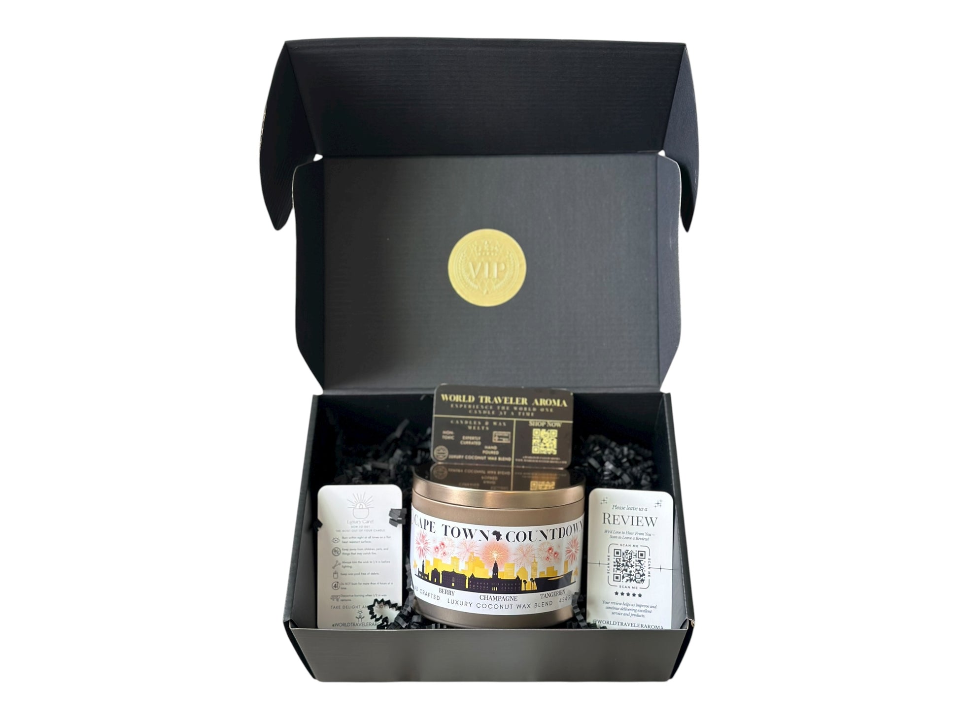 A black gift box with a gold VIP sticker on the lid inside the box a gold candle tin labeled "Cape Town Countdown" with a candle care card instructions, a please review us card, and World Traveler Aroma business card on a white background.