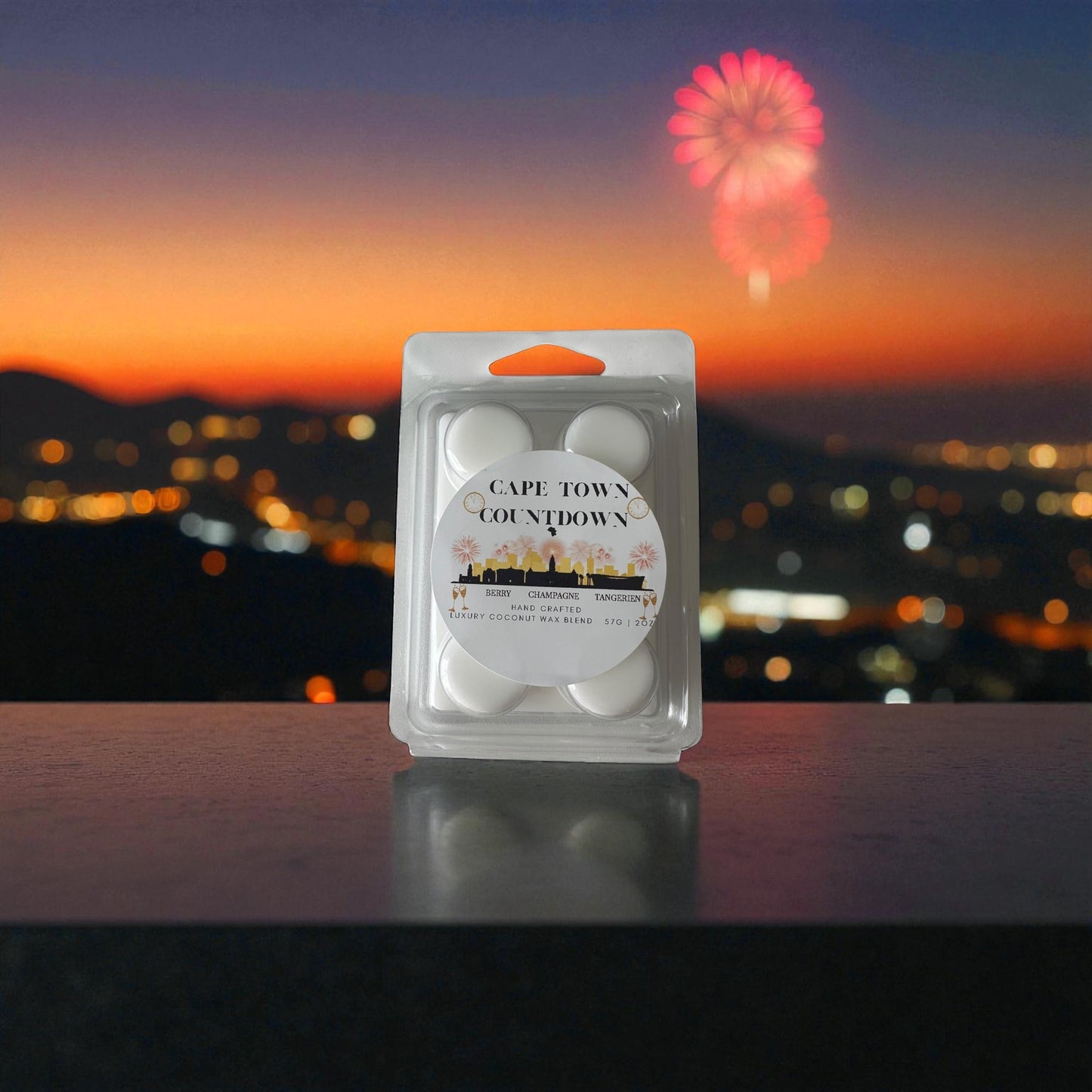 A new year wax melt labeled "Cape Town Countdown" sitting on a balcony ledge over looking Cape Towns city scape at dusk with fireworks in the night sky.