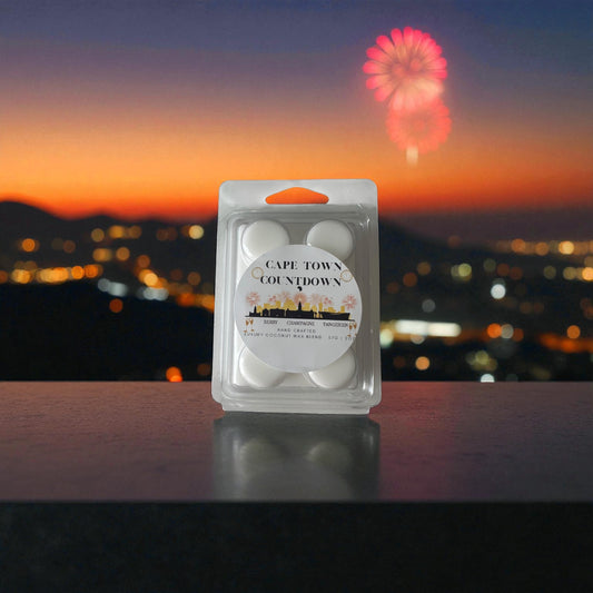 A new year wax melt labeled "Cape Town Countdown" sitting on a balcony ledge over looking Cape Towns city scape at dusk with fireworks in the night sky.