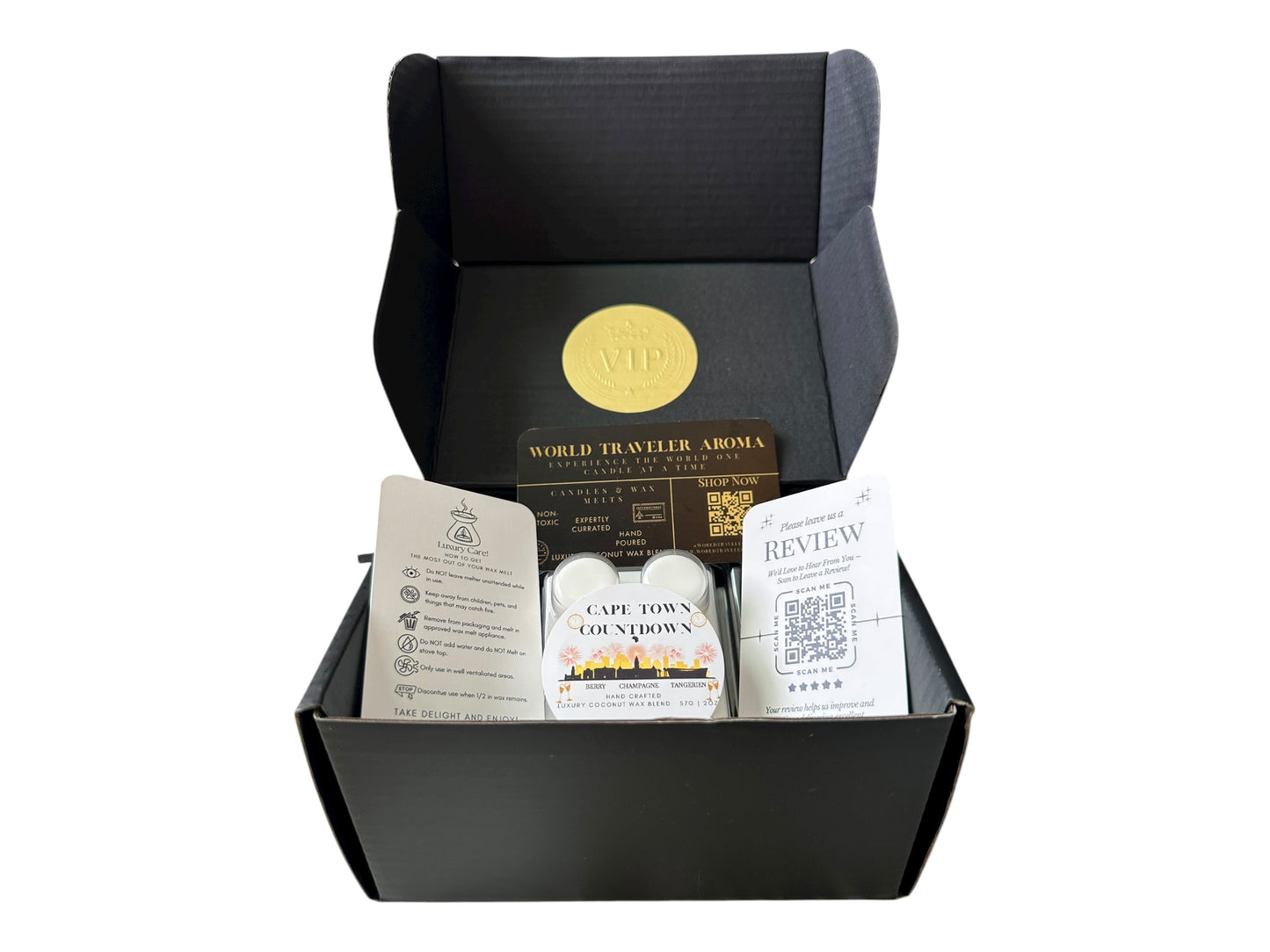 A black gift box with a gold VIP sticker on the lid inside the box a white coconut wax melt labeled "Cape Town Countdown" a wax melt care instructions card, a please review us card, and a World Traveler Aroma business Card on a white background.