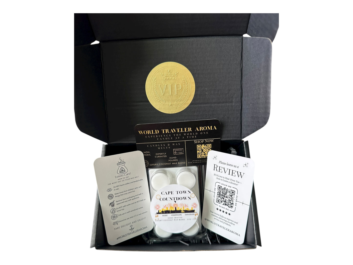 A black gift box with a gold VIP sticker on the lid inside the box a white coconut wax melt labeled "Cape Town Countdown" a wax melt care instructions card, a please review us card, and a World Traveler Aroma business Card on a white background.