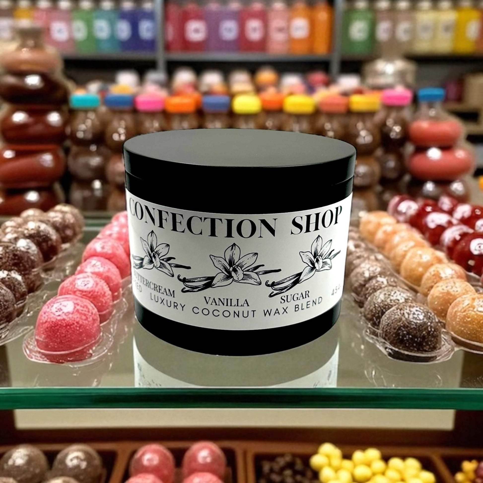 Black candle tin labled confection shop on a glass counter top surrounded by candy and sweets.