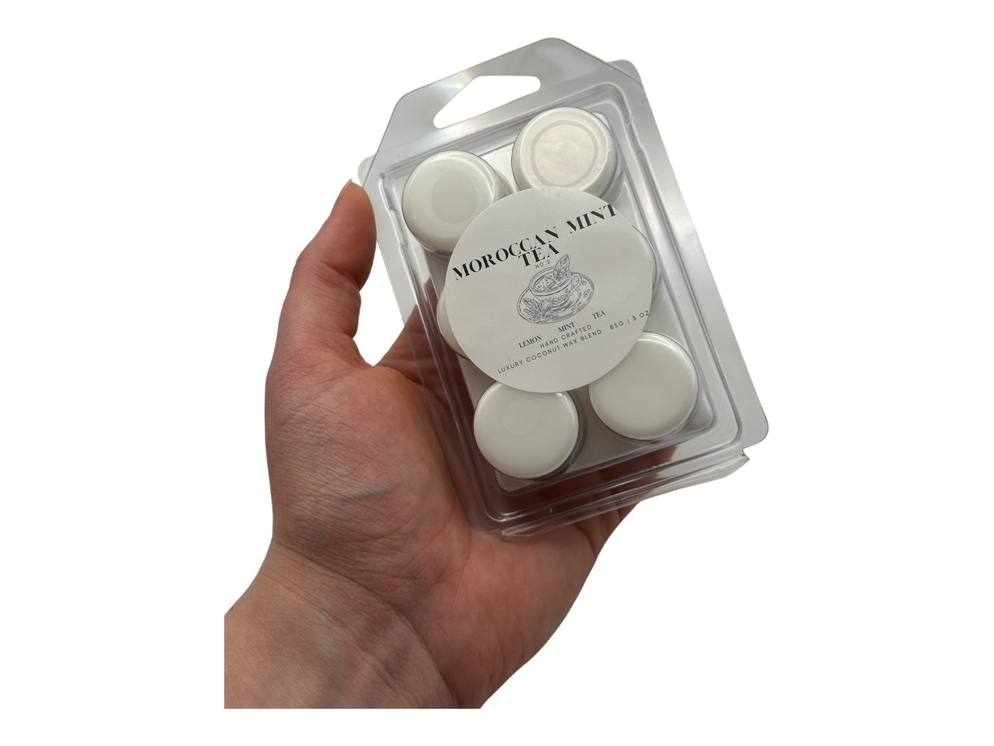 A hand holding white wax melt labeled Moroccan Mint Tea front view.