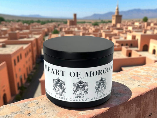 A black candle tin labeled Heart of Morocco resting on a ledge overlocking a city in Morocco. 