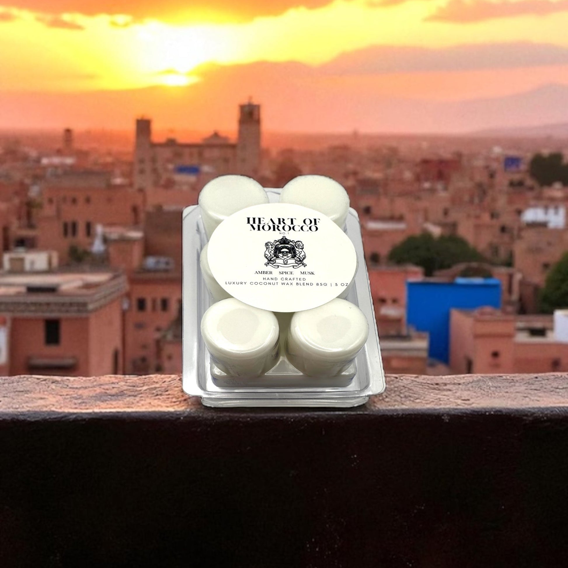 A white wax melt in a clear clamshell labeled Heart of Morocco resting on a concrete ledge overlooking a city in Morocco. 