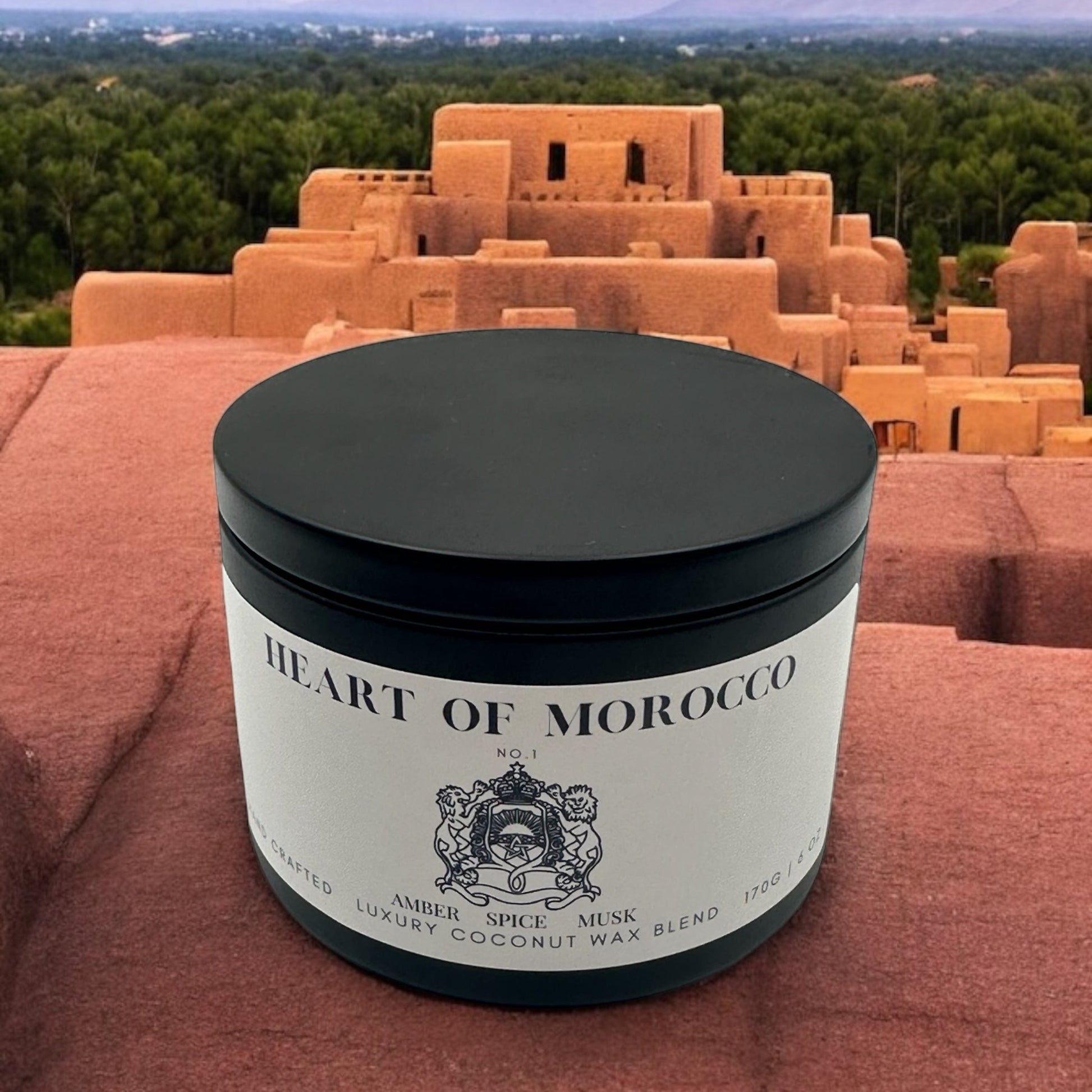A black candle tin labeled Heart of Morocco resting on a concrete ledge over looking a city in Morocco.