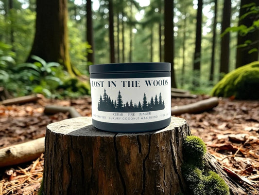 A black candle tin resting on a tree trunk labeled Lost in the Woods on a background of a forest.