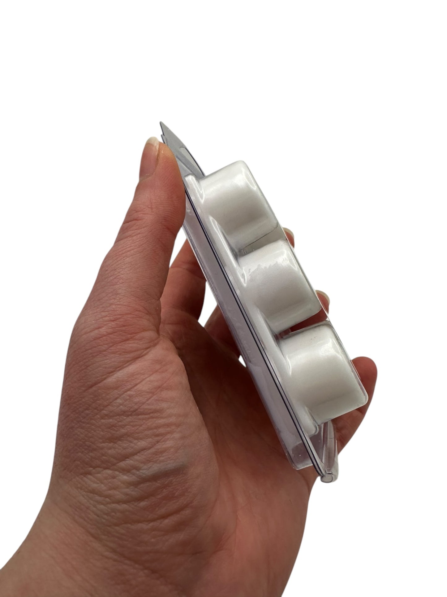 A hand holding white wax melts in a plastic clamshell on a white background.