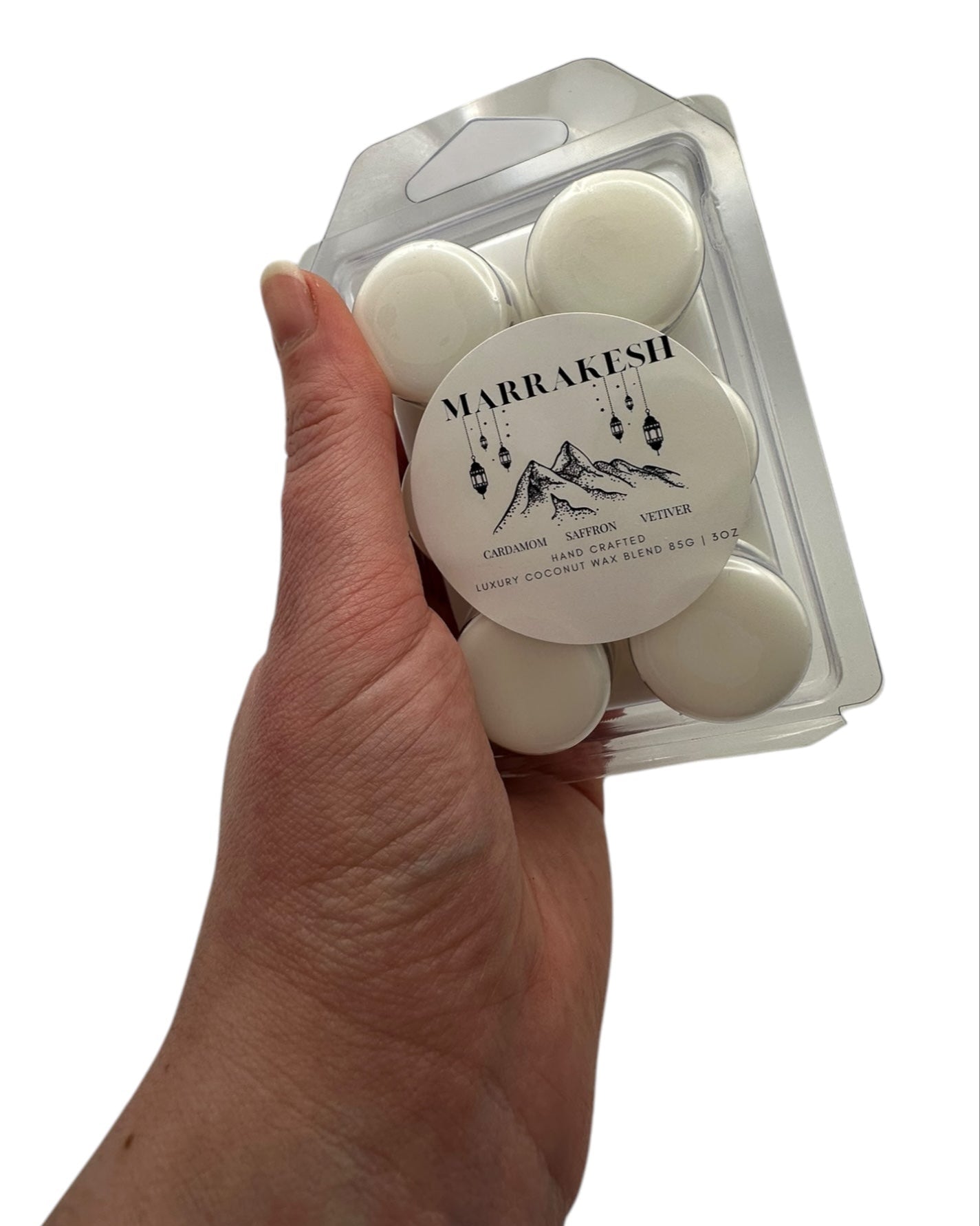 A hand holding white wax melts labeled "Marrakesh" on a white background. 