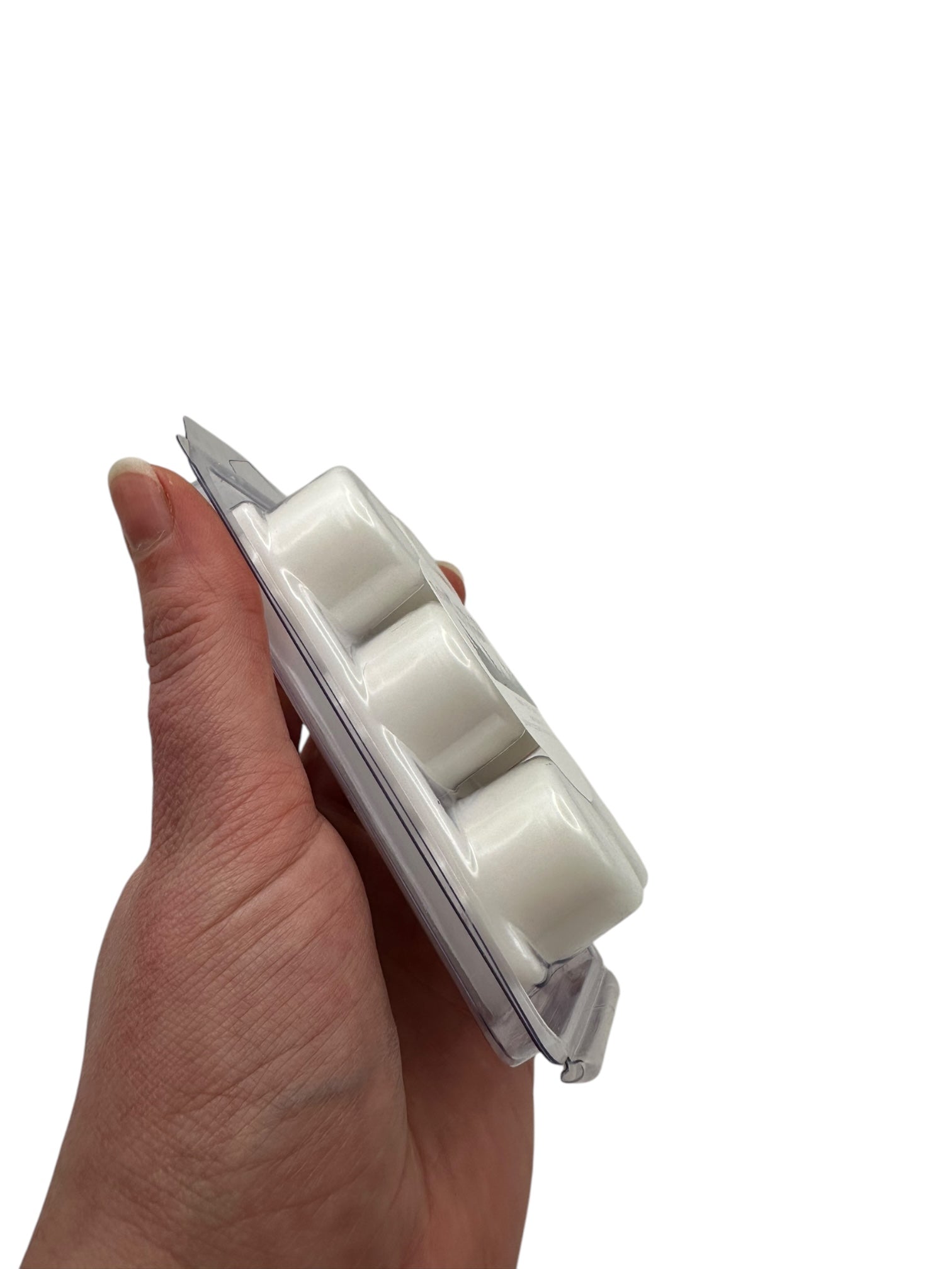 A hand holding a white wax melts in a plastic clamshell on a white background. 