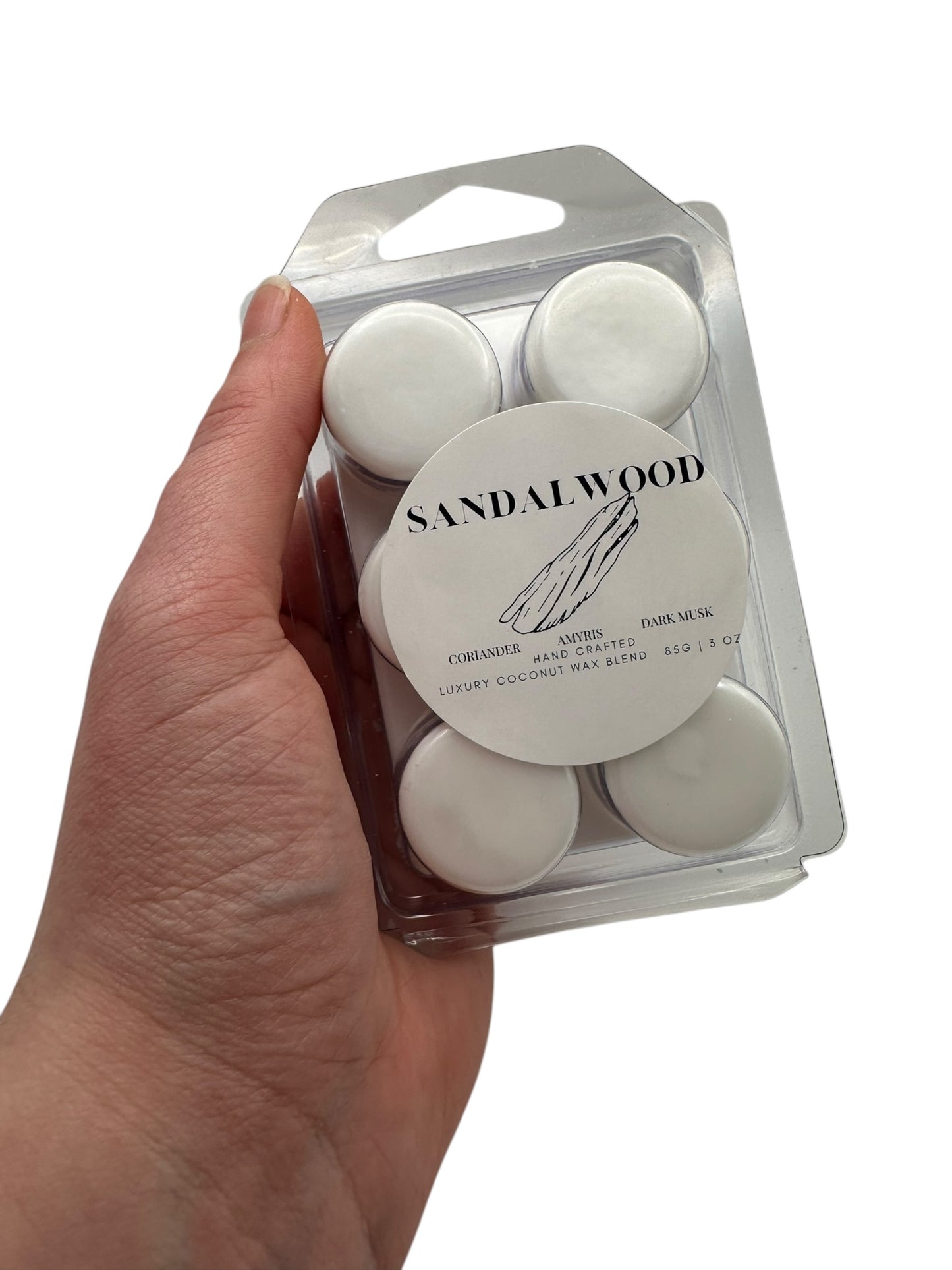 A hand holding a  plastic clamshell wax melts labeled "Sandalwood" on a white background.