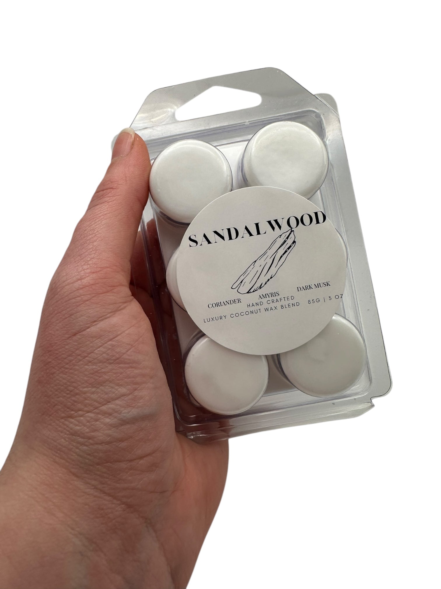 A hand holding a  plastic clamshell wax melts labeled "Sandalwood" on a white background.