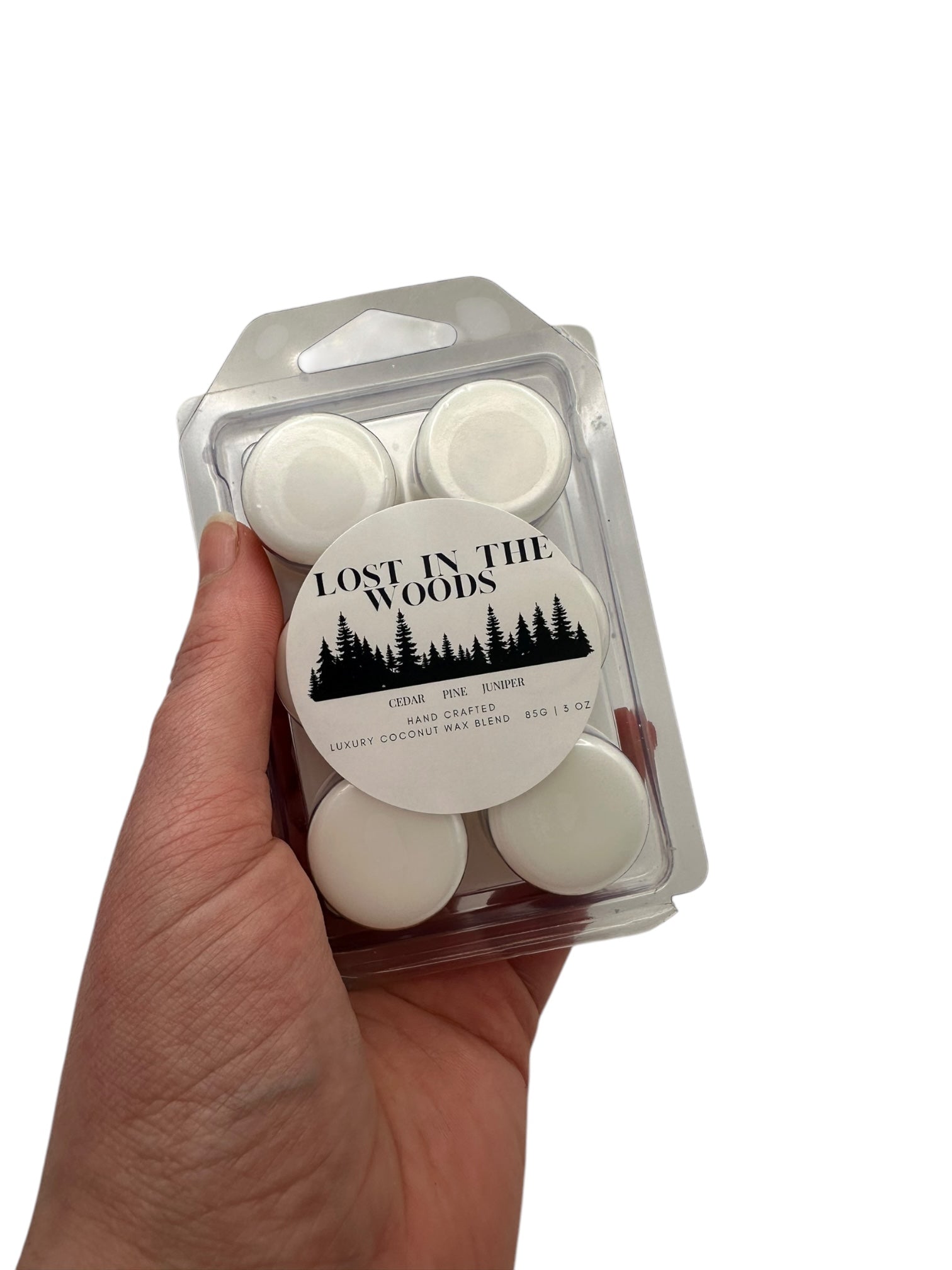 A hand holding a plastic clamshell white wax melts labeled "Lost in the Woods" on a white background. 
