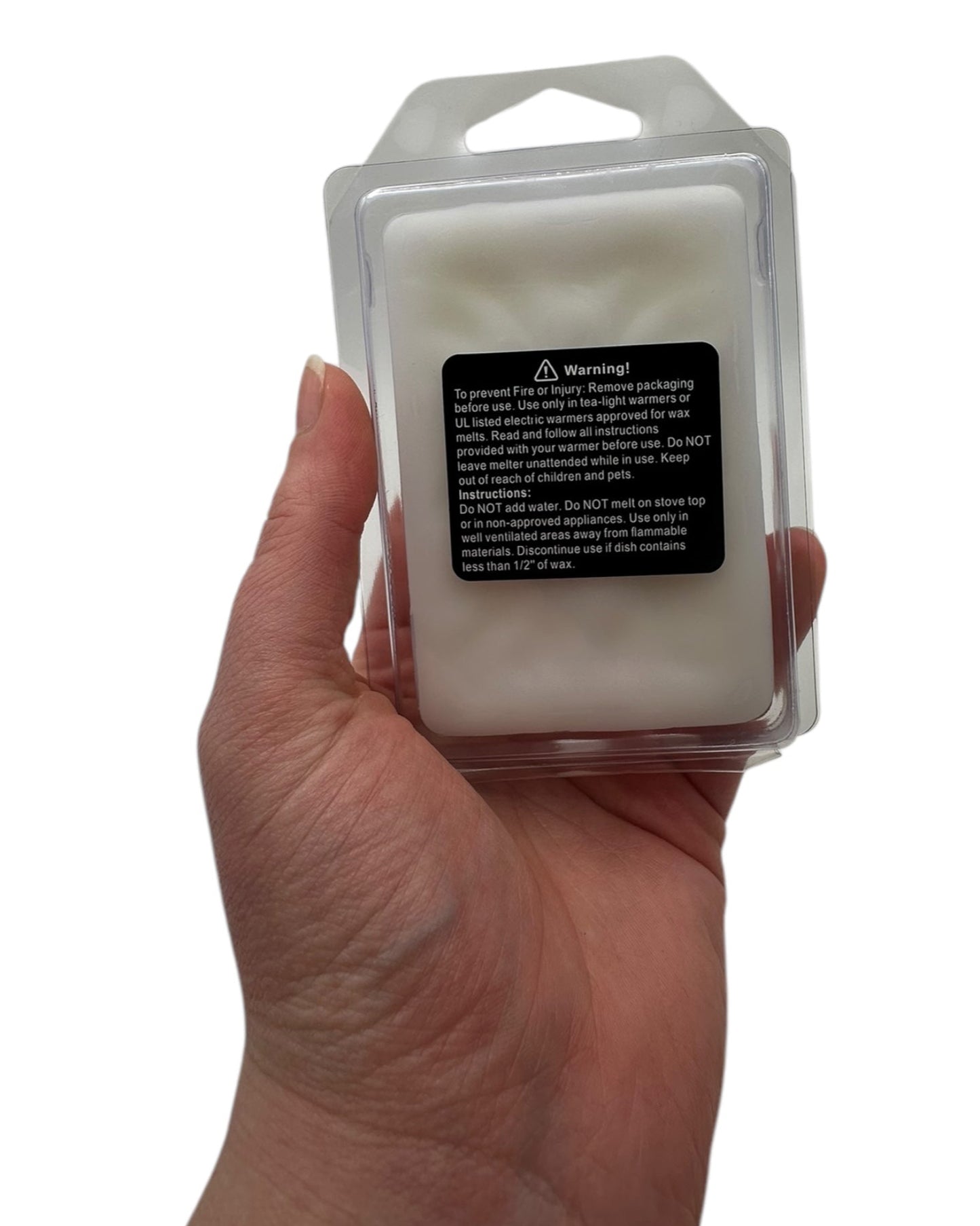 A hand holding a white wax melt with a safety warning label on a white background. 