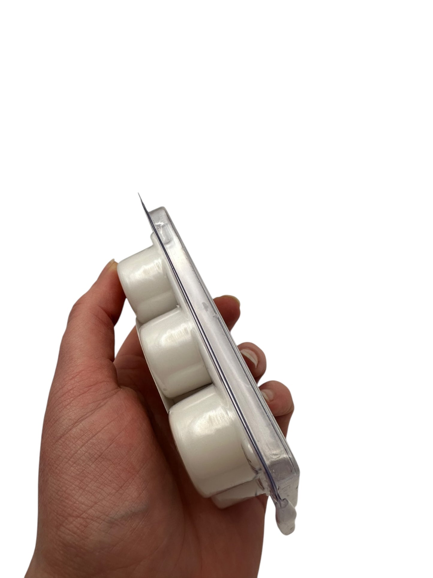 A hand holding a white wax melt in plastic clamshell on a white background.