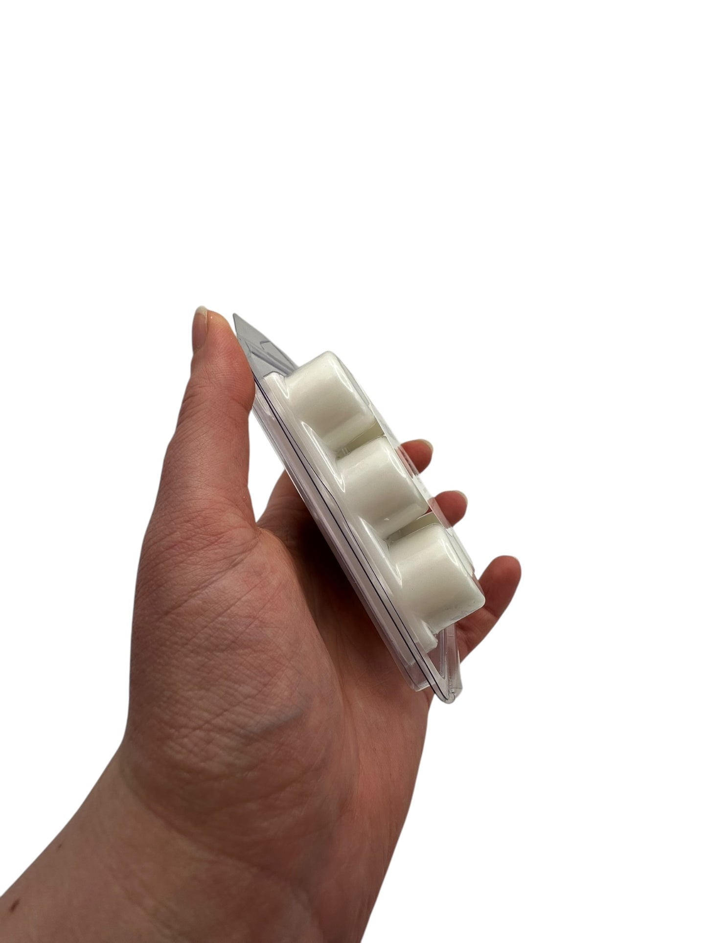 A hand holding plastic clamshell with white wax melts on a white background.