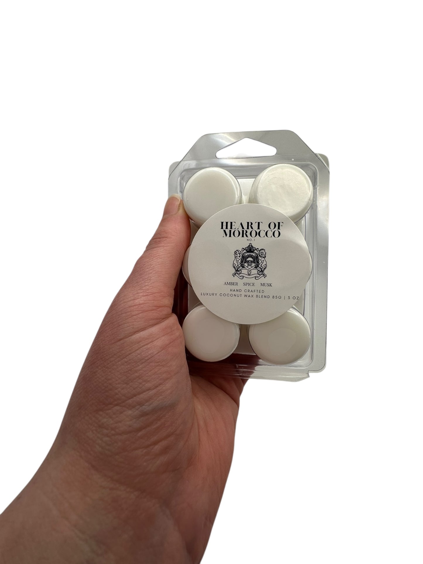 A hand holding a plastic clamshell with white wax melts labeled "Heart of Morocco" on a white background.