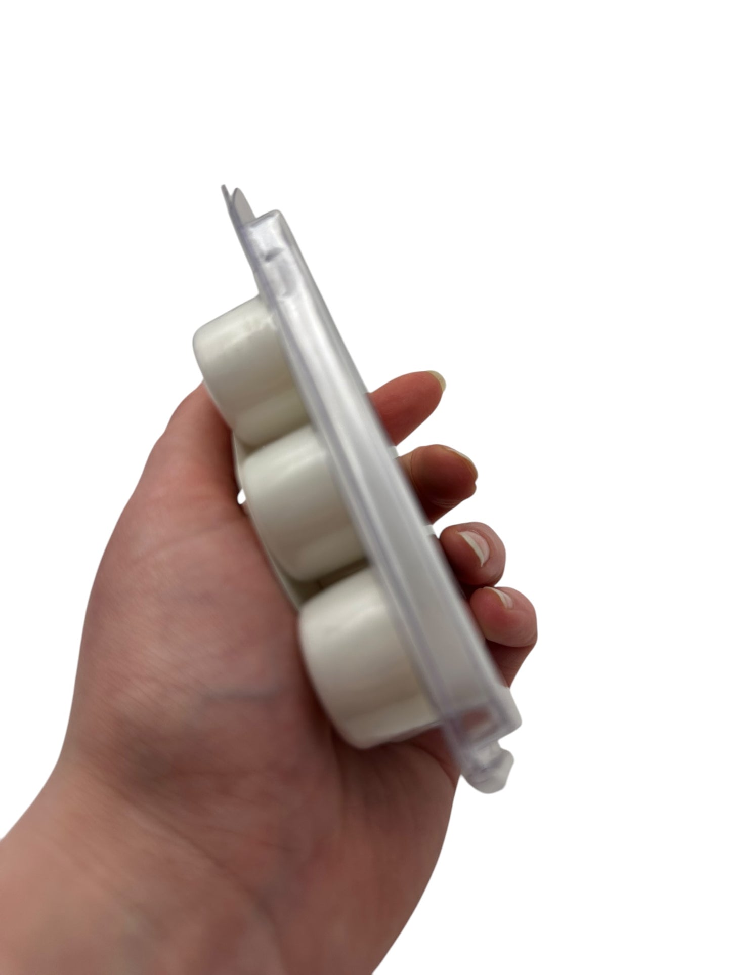 A hand holding a plastic clamshell of white wax melts on a white background.