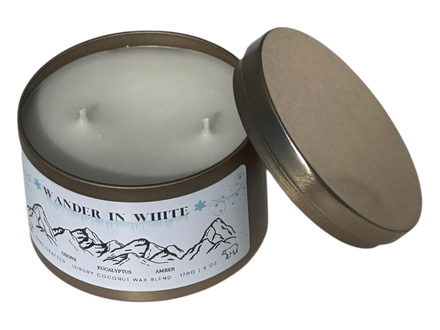 A gold candle tin labeled "Wander in White" with lid removed displaying two candle wicks on top on a white background.