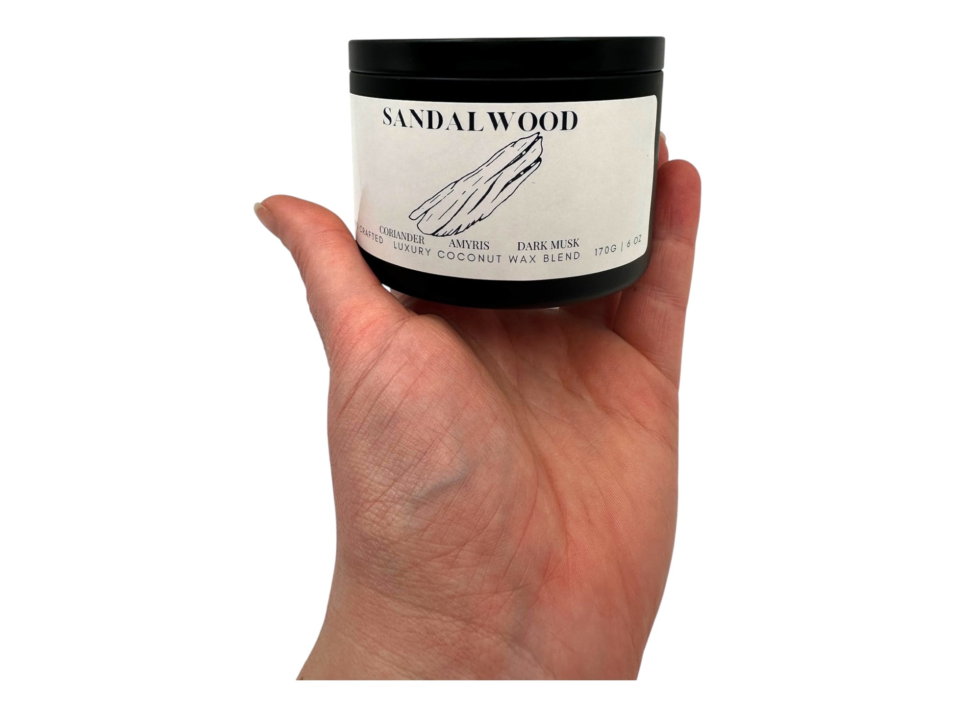 A hand holding a black candle tin labeled "Sandalwood" on a white background.