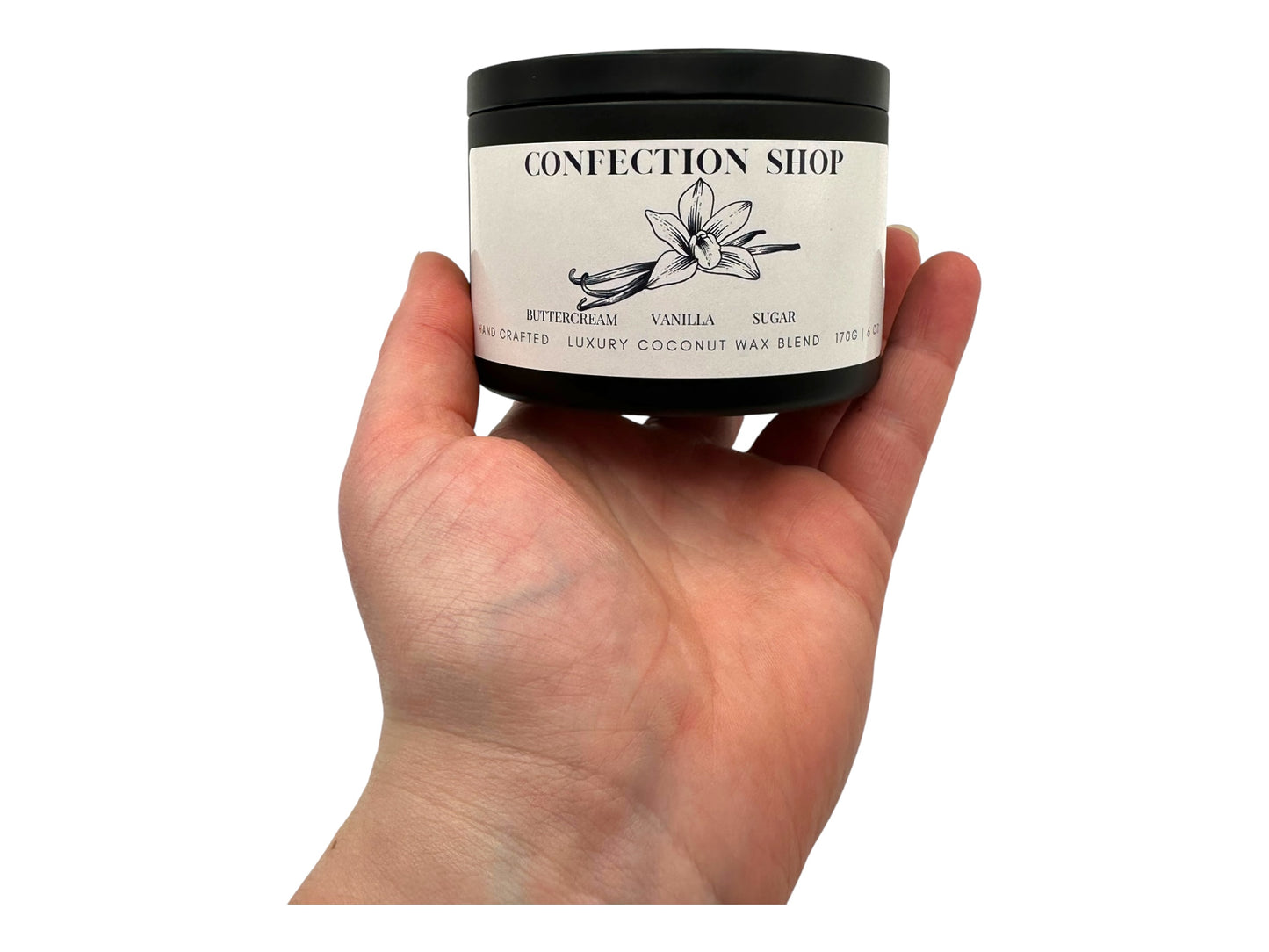 A hand holding a black candle tin labeled "Confection Shop" on a white background. 